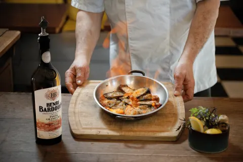 Un chef dresse une poêlée de fruits de mer à côté d'une bouteille de Pastis Henri Bardouin