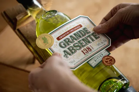 Mains tenant une bouteille de Grande Absente