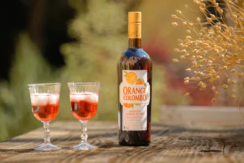 Deux verres de spritz rosé et une bouteille de liqueur Orange Colombo sur une table en bois