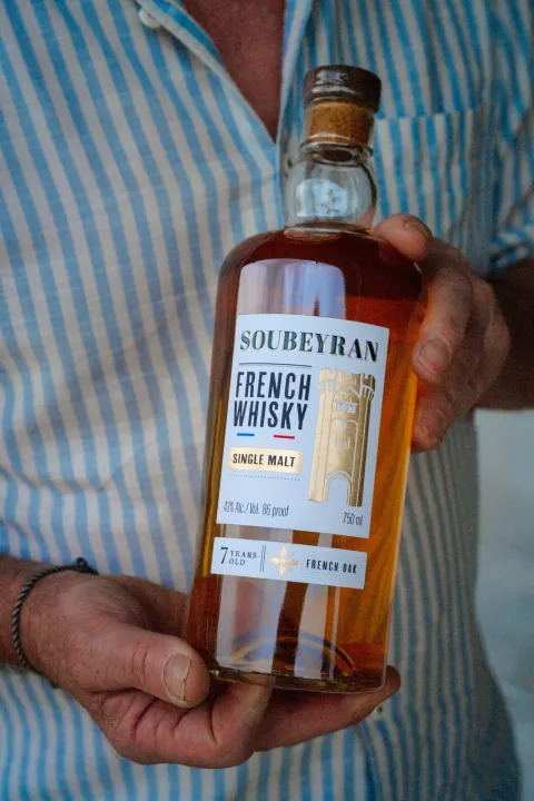 Bouteille de whisky Soubeyran tenue contre une chemise rayée