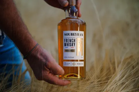 Bouteille de whisky Soubeyran tenue au-dessus des épis d'orge