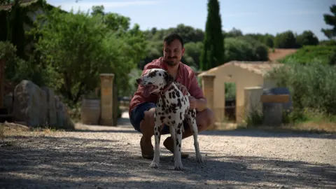 Propriétaire d'un gîte avec son chien devant le portail